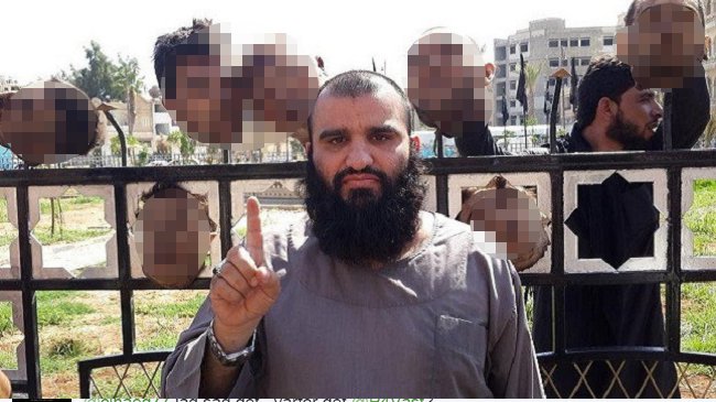 IS-krigare gör IS-hälsning med avhuggna huvuden i bakgrunden.