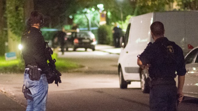Tungt beväpnad polis står och bevakar innanför det avspärrade området. Foto: Nyheter Idag